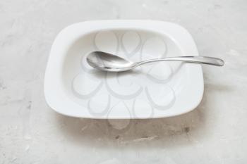 square white bowl with white spoon on gray concrete board