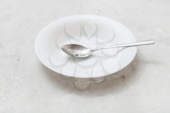 white deep plate with steel spoon on gray concrete board