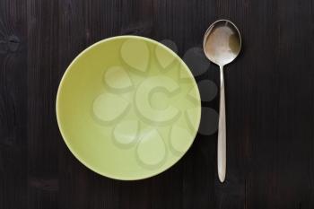 top view of one green bowl and spoon on dark brown table