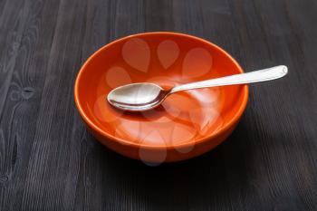 one orange bowl with spoon on dark brown board