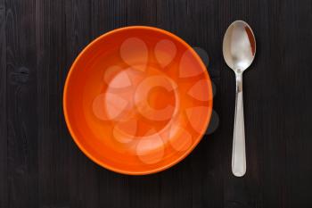 top view of one orange bowl and spoon on dark brown table