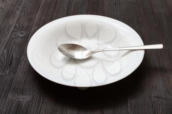 one white deep plate with spoon on dark brown table