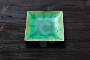 one green square saucer on dark brown table