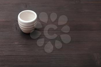 food concept - white ceramic cup for sake (ochoko, choko) on dark brown wooden board