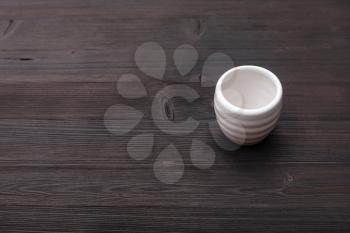 food concept - white ceramic cup for sake (ochoko, choko) on dark brown wooden table