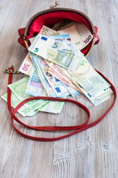 various euro banknotes fall out from red leather handbag on wooden table