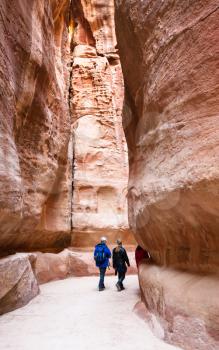 PETRA, JORDAN - FEBRUARY 21, 2012: tourists walk in narrow Al Siq passage to Petra town in winter. Rock-cut town Petra was established about 312 BC as the capital city of the Arab Nabataean