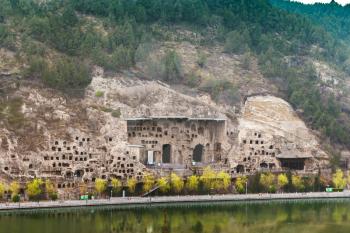 LUOYANG, CHINA - MARCH 20, 2017: View of Grottoes on West Hill of Chinese Buddhist monument Longmen Grottoes (Longmen Caves, Dragon's Gate) from the east bank of the Yi River in spring season