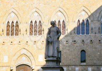 travel to Italy - statue of medieval Italian archdeacon Sallustio Bandini on Piazza Salimbeni and wall of Gothic style Palazzo Salimbeni in Siena city in winter