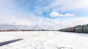 blue cloudy sky over frozen Neva river with polynya, Dvortsovaya Embankment and Peter and Paul Fortress in Saint Petersburg city in March