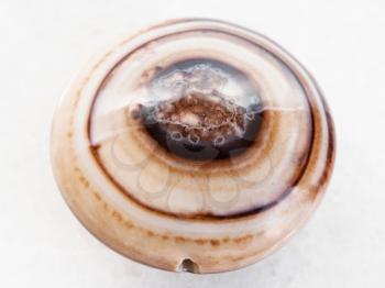 macro shooting of natural mineral rock specimen - polished bead from banded Agate gemstone on white marble background