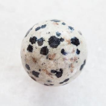 macro shooting of natural mineral rock specimen - bead from Dalmatian Jasper gemstone on white marble background