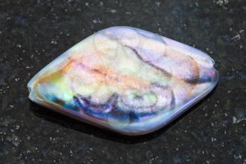 macro shooting of natural mineral rock specimen - bead from Abalone (haliotis) shell on dark granite background