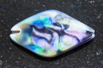 macro shooting of natural mineral rock specimen - iridescent bead from Abalone (haliotis) shell on dark granite background