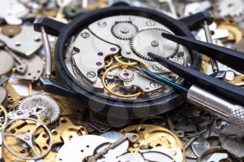 watchmaker workshop - screwdriver and tweezers on open mechanical watch on heap of clock spare parts close up