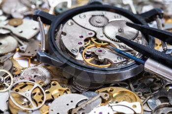 watchmaker workshop - screwdriver and tweezers on open watch on pile of clock spare parts close up