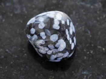 macro shooting of natural mineral rock specimen - polished snowflake obsidian gemstone on dark granite background
