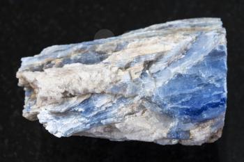 macro shooting of natural mineral rock specimen - rough kyanite stone on dark granite background from Keivy region, Kola Peninsula, Russia