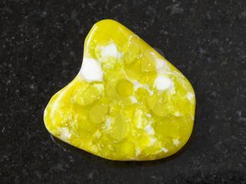 macro shooting of natural mineral rock specimen - tumbled yellow Lizardite gemstone on dark granite background