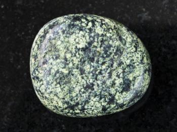 macro shooting of natural mineral rock specimen - tumbled serpentine gemstone on dark granite background