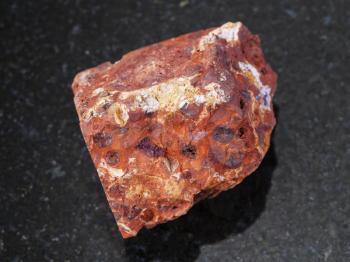 macro shooting of natural mineral rock specimen - rough red bauxite stone on dark granite background