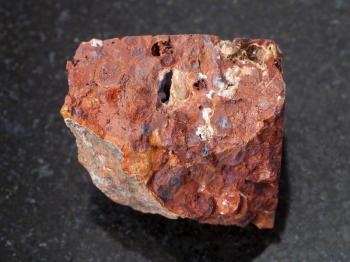 macro shooting of natural mineral rock specimen - raw red bauxite stone on dark granite background