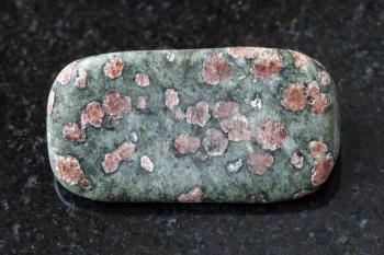 macro shooting of natural mineral rock specimen - tumbled Eclogite gemstone on dark granite background from Salma region, Kola peninsula, Russia