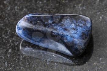 macro shooting of natural mineral rock specimen - tumbled dumortierite gem on dark granite background