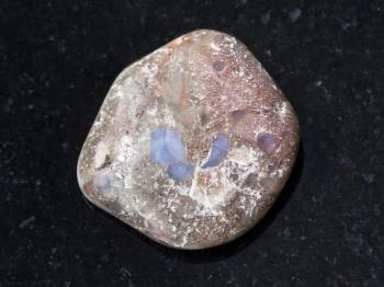 macro shooting of natural mineral rock specimen - tumbled porphyry gemstone on dark granite background