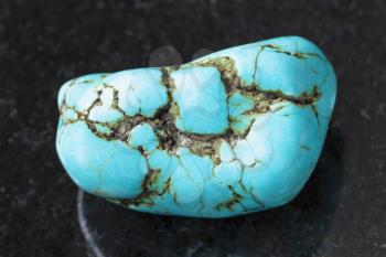 macro shooting of natural mineral rock specimen - tumbled blue howlite (turquenite) gem stone on dark granite background