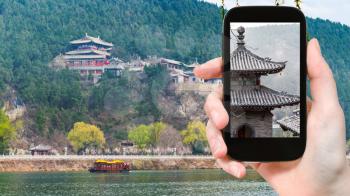 travel concept - tourist photographs pagoda on East Hill of Chinese Buddhist monument Longmen Grottoes in spring on smartphone