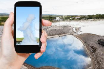 travel concept - tourist photographs pool of The Geisyr (The Great Geysir) in Haukadalur hot spring area in Iceland in september on smartphone