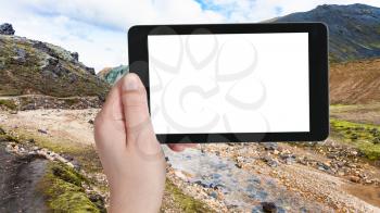 travel concept - tourist photographs river in Graenagil canyon, Landmannalaugar area of Fjallabak Nature Reserve in Highlands region of Iceland on tablet with cut out screen for advertising logo