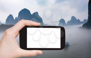 travel concept - tourist photograps boats in fog over river near Xingping town in Yangshuo county in China in spring morning on smartphone with cut out screen for advertising logo