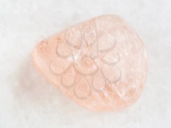 macro shooting of natural mineral rock specimen - tumbled morganite (pink beryl) gemstone on white marble background from Ural Mountains, Russia