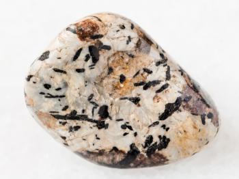 macro shooting of natural mineral rock specimen - black aegirine in tumbled Sanidine and nepheline stone on white marble background from Lovozero Massif, Kola peninsula, Russia