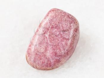 macro shooting of natural mineral rock specimen - tumbled rhodonite gem on white marble background from Ural Mountains
