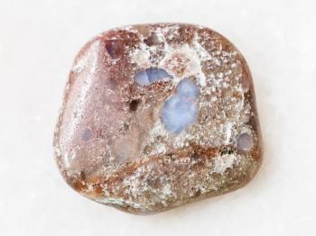macro shooting of natural mineral rock specimen - tumbled porphyry gemstone on white marble background