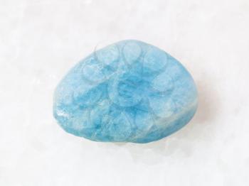 macro shooting of natural mineral rock specimen - tumbled aquamarine (blue beryl) gem stone on white marble background from Brazil