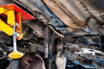 repairing of corrugation muffler of exhaust system in car workshop - repairer welds the silencer on car by argon welding