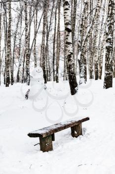 wooden bench and snowman in birch grove of Timiryazevskiy park in Moscow city in winter
