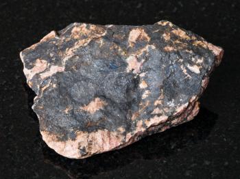 macro shooting of natural mineral - rough Rhodonite gemstone on black granite from Ural Mountains