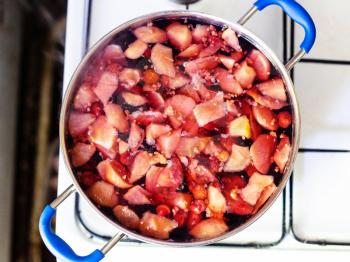 top view of cooking of local non-alcoholic sweet drink Kompot (compote) from fresh apricot fruits, raspberries, cherries in rural kitchen