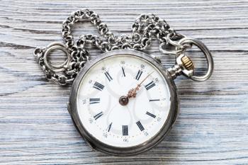 two minutes to twelve o'clock on old pocket watch with chain on gray wooden background