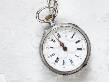 two minutes to twelve o'clock on antique pocket watch on white concrete background