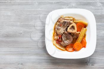 top view of cooked italian dish Ossobuco in white plate on gray wooden board with blank copyspace