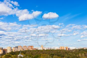 many white clouds in blue sky over apartment houses and urban park in sunny autumn day