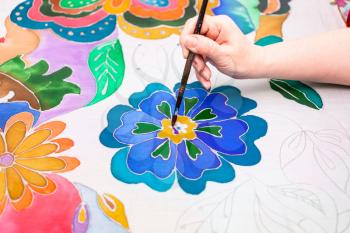 artist paints flower on white silk canvas in cold contour batik technique