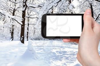 travel concept - tourist photographs of snowman on snow-covered meadow in oak grove of city park in winter in Moscow city on smartphone with empty cutout screen with blank place for advertising
