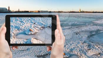 travel concept - tourist photographs of ice-bound Neva river near Dvortsovaya Embankment in Saint Petersburg city in Russia on smartphone in spring